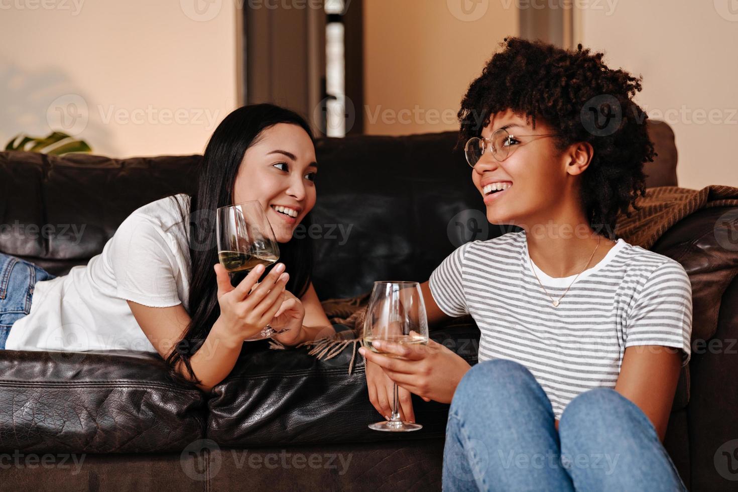 Mädchen in weißen T-Shirts lächeln, plaudern und halten Gläser Weißwein in der Hand. foto