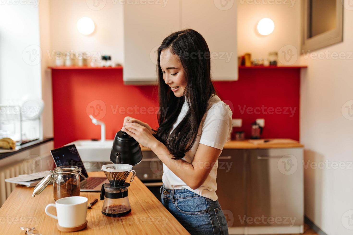 Attraktives dunkelhaariges Mädchen in Jeans gießt fleißig Wasser in die Kaffeekanne foto