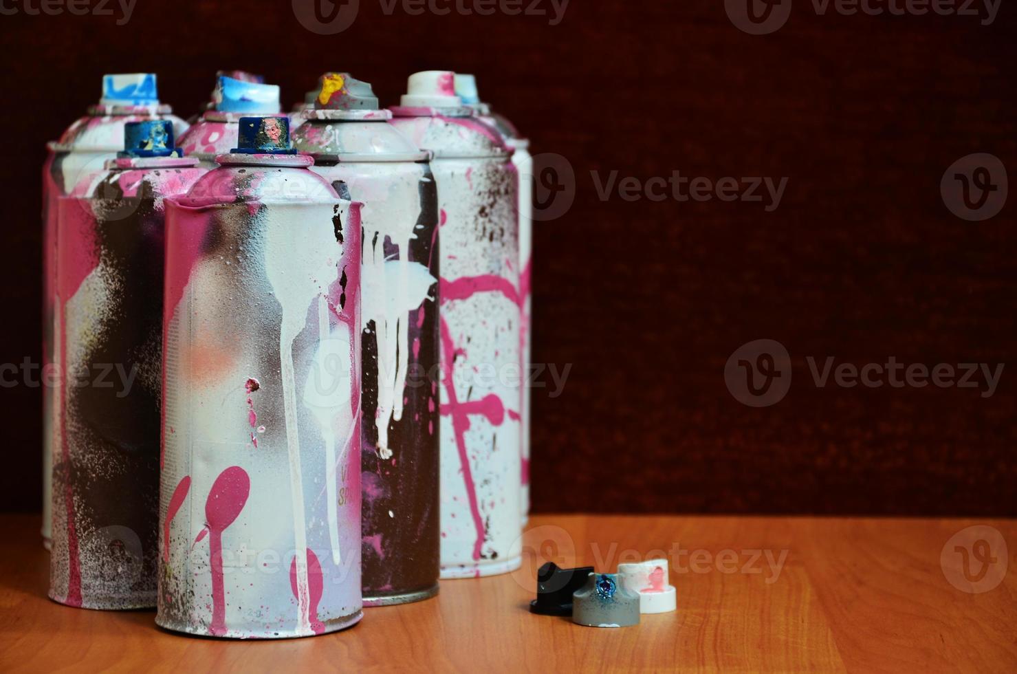 Stillleben mit einer großen Anzahl gebrauchter bunter Spraydosen mit Aerosolfarbe, die auf der behandelten Holzoberfläche in der Graffiti-Werkstatt des Künstlers liegen. schmutzige und befleckte Dosen für Sprühkunst foto