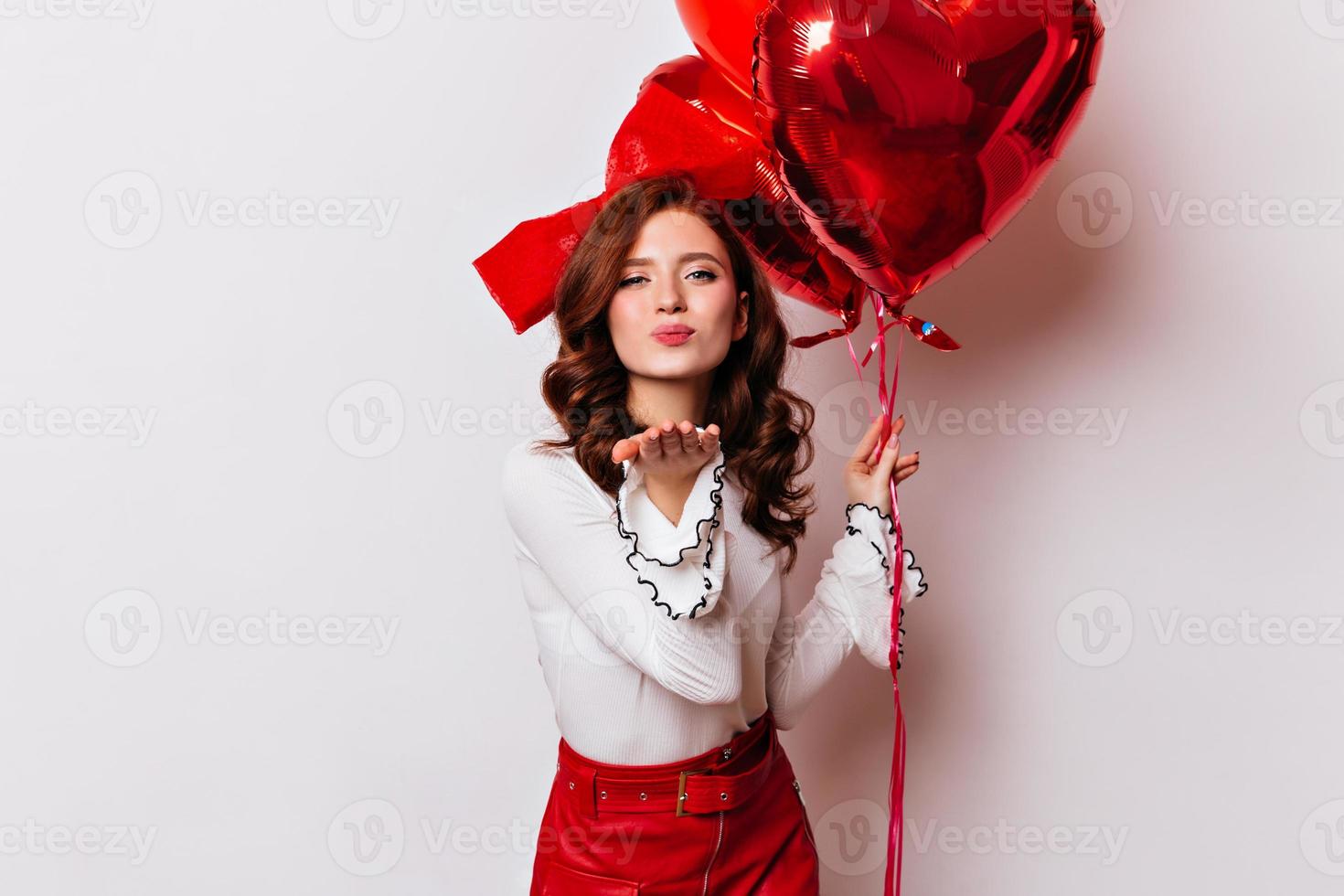 sorgloses Ingwermädchen, das Luftkuss sendet. studiofoto der fröhlichen dame mit luftballons isoliert auf weiß. foto