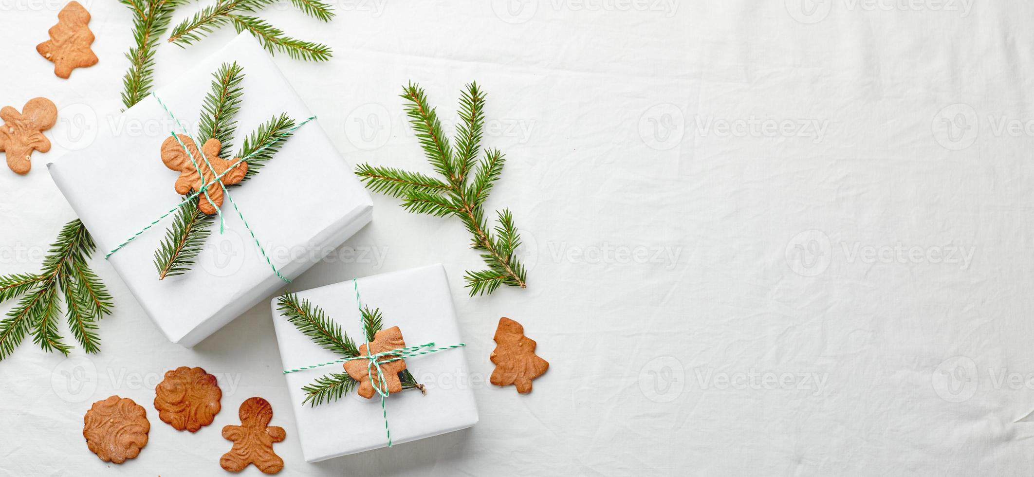 weihnachtsgeschenke eingewickelt in weißes papier und verziert mit fichtenzweigen und lebkuchenplätzchen foto