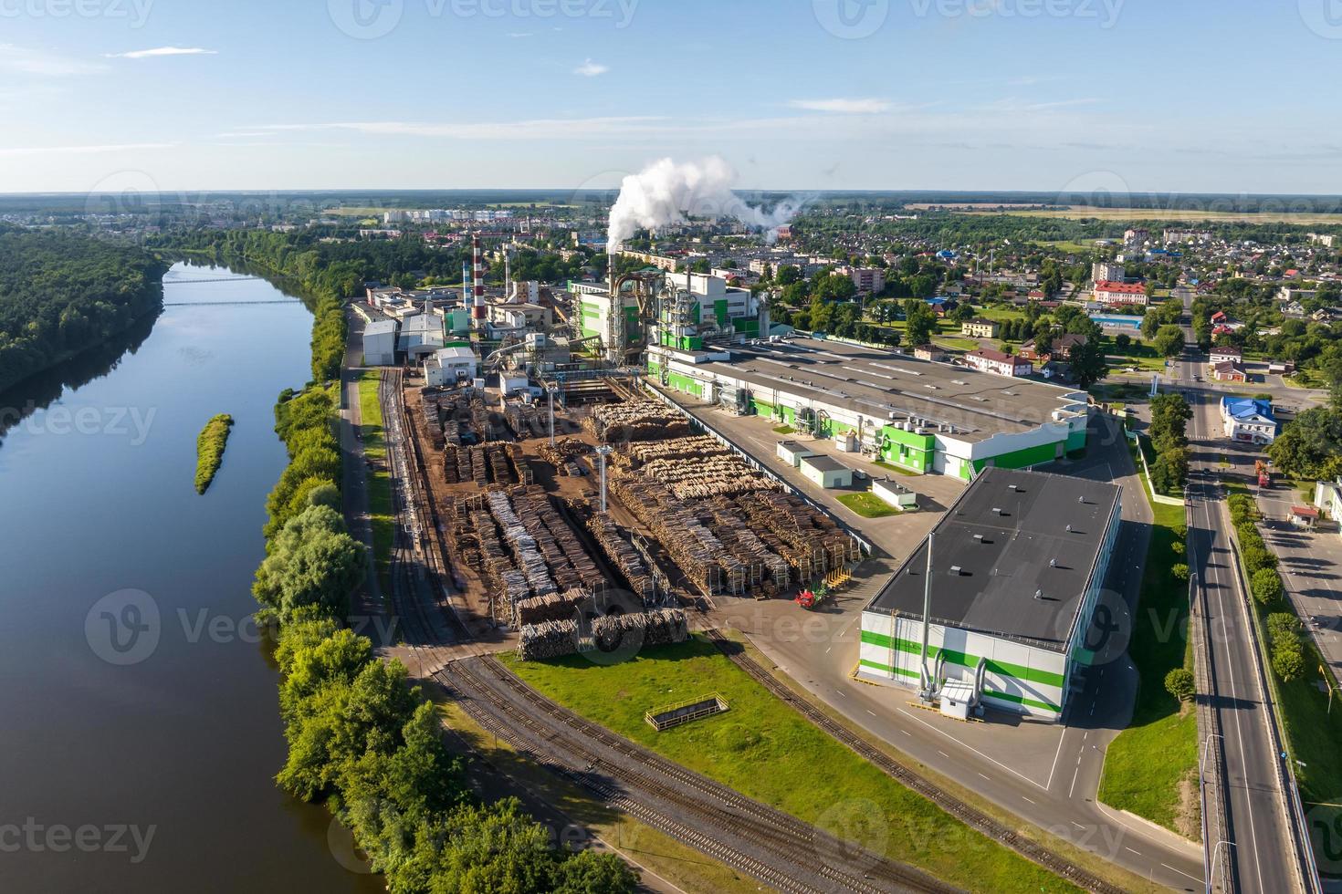 Luftpanoramablick auf Rauchrohre einer Holzverarbeitungsfabrik am Ufer eines breiten Flusses foto