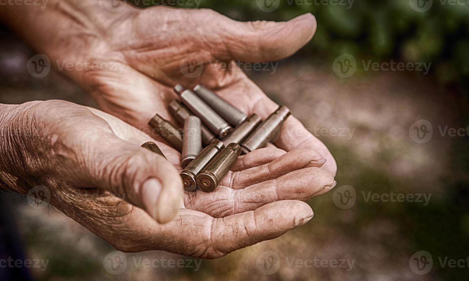 leere Patronen für einen Karabiner oder ein Gewehr in den faltigen Händen eines älteren Rentners. Das Armeethema ist gegen einen bewaffneten Konflikt, Krieg oder Schießereien. verschwommener Fokus. foto