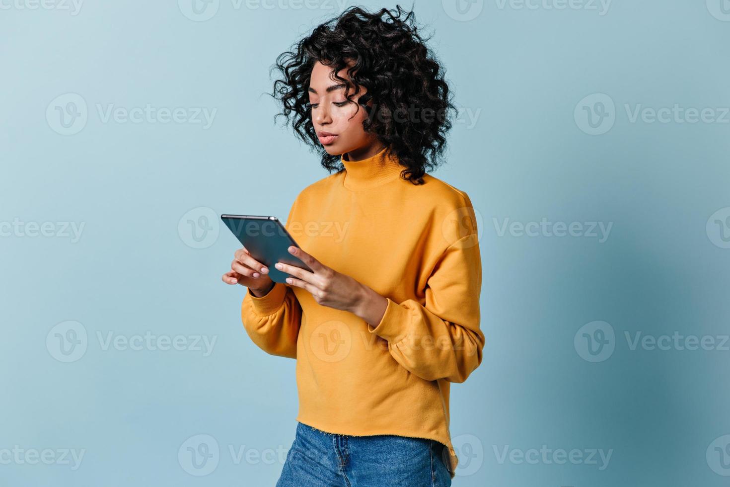attraktive junge Frau mit digitalem Tablet. Studioaufnahme eines Mischlingsmädchens im gelben Sweatshirt. foto