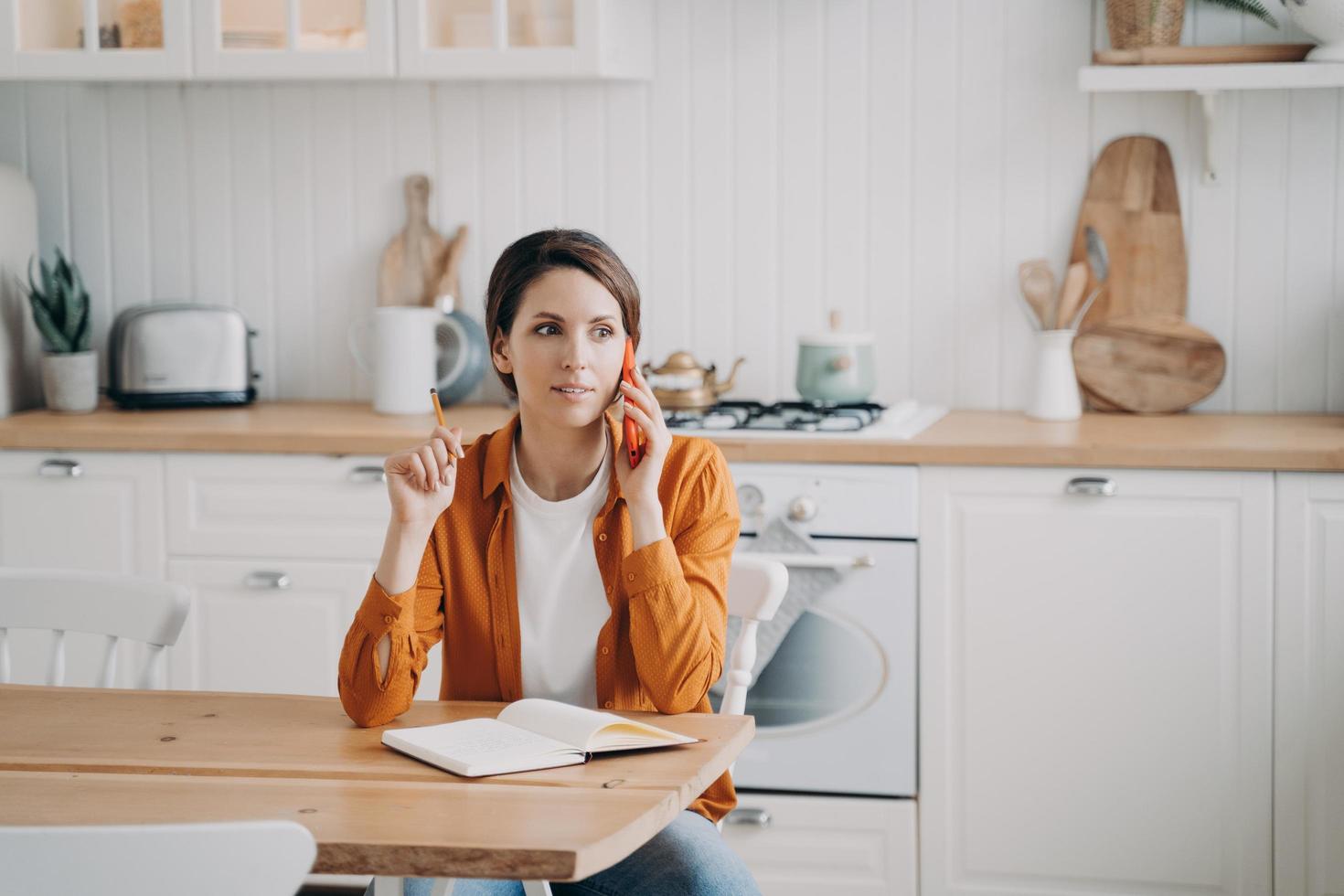 frau, die den kundendienst telefonisch anruft und zu hause in der küche sitzt. häusliches Leben, Remote-Job foto