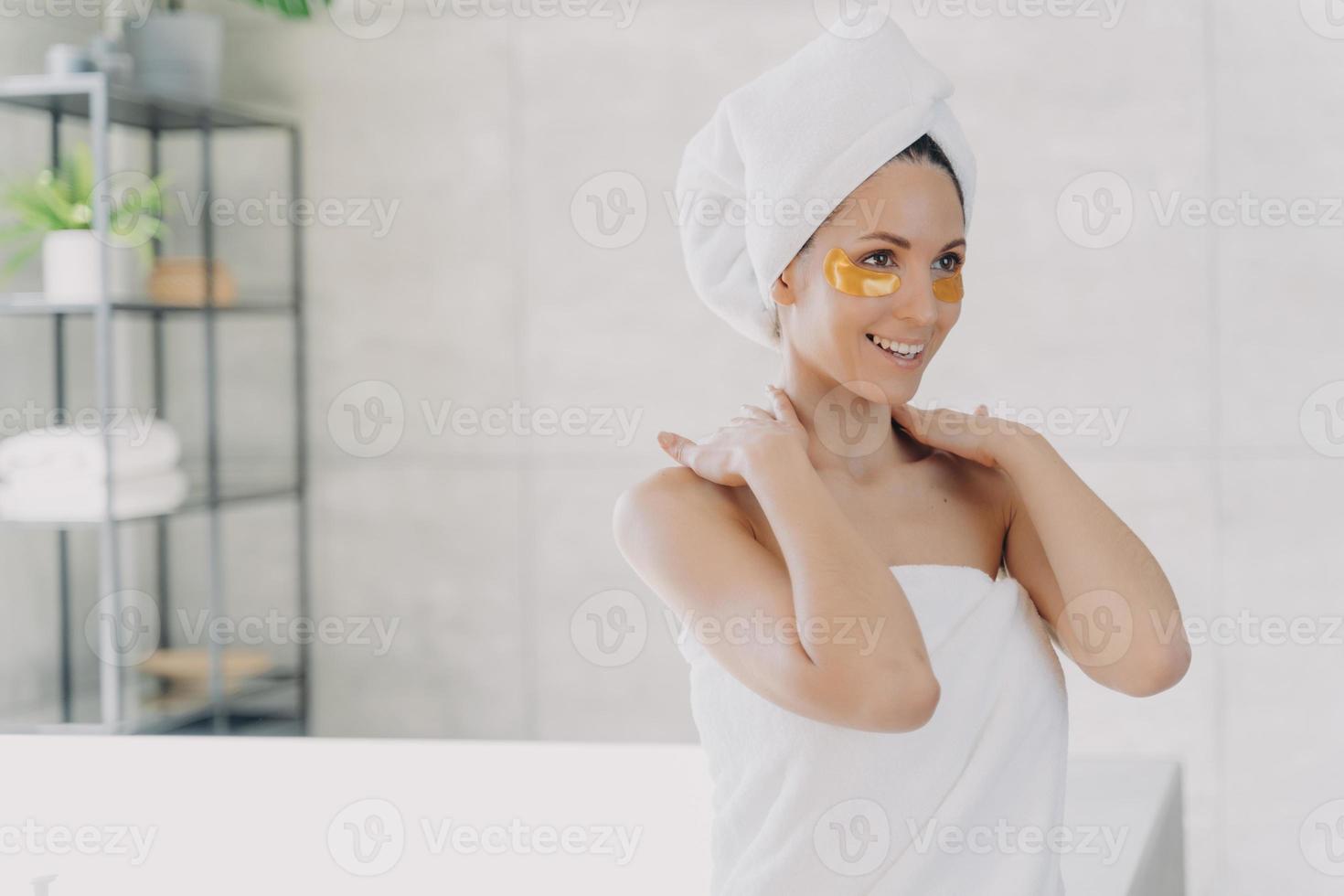 frau mit hydrogel-augenflecken auf der gesichtshaut, die nach der dusche die hautpflegeroutine im badezimmer genießt foto