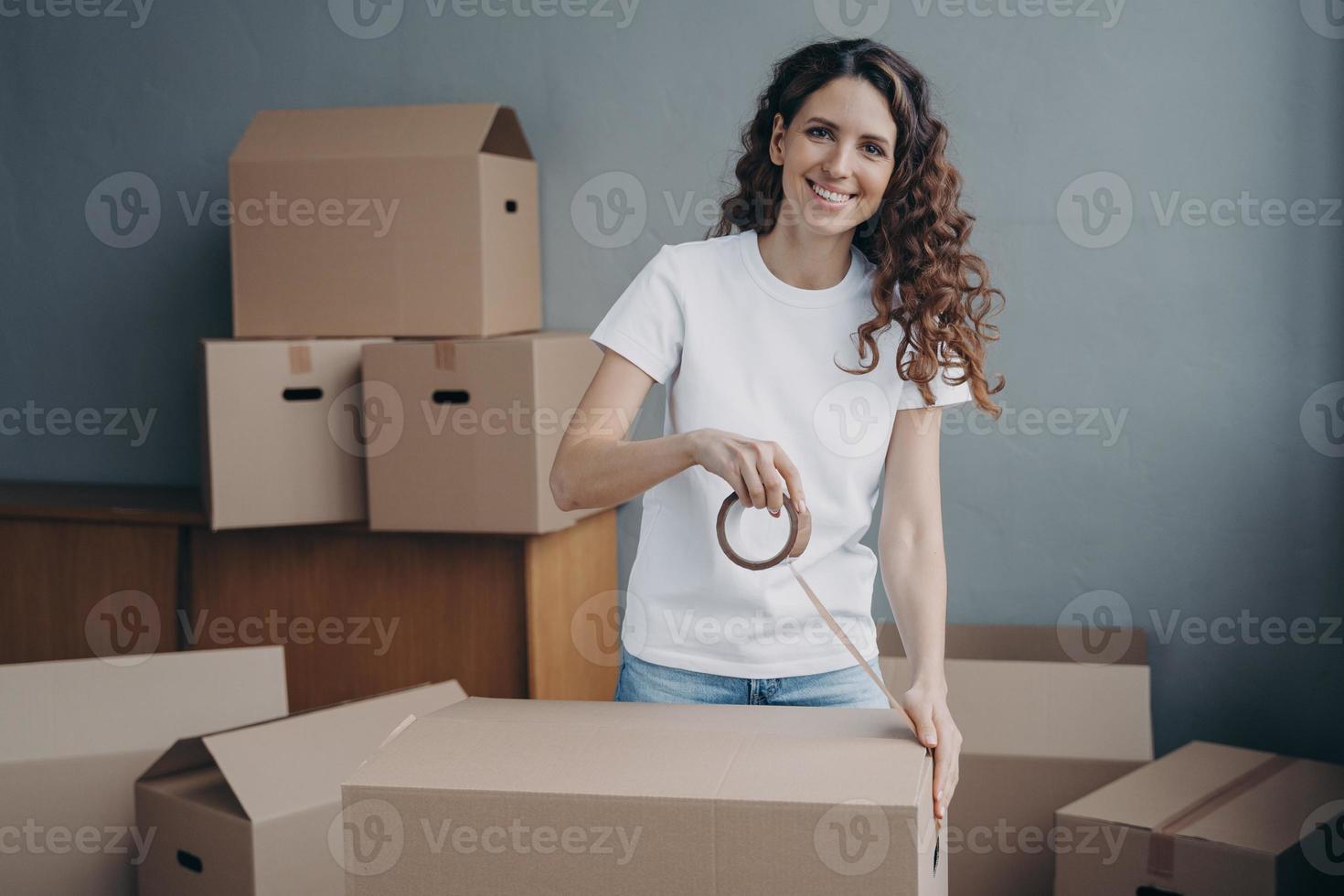 lächelnde Spanierin, die Sachen in Kartons verpackt, mit Klebeband. Lieferservice, Umzugsservice foto