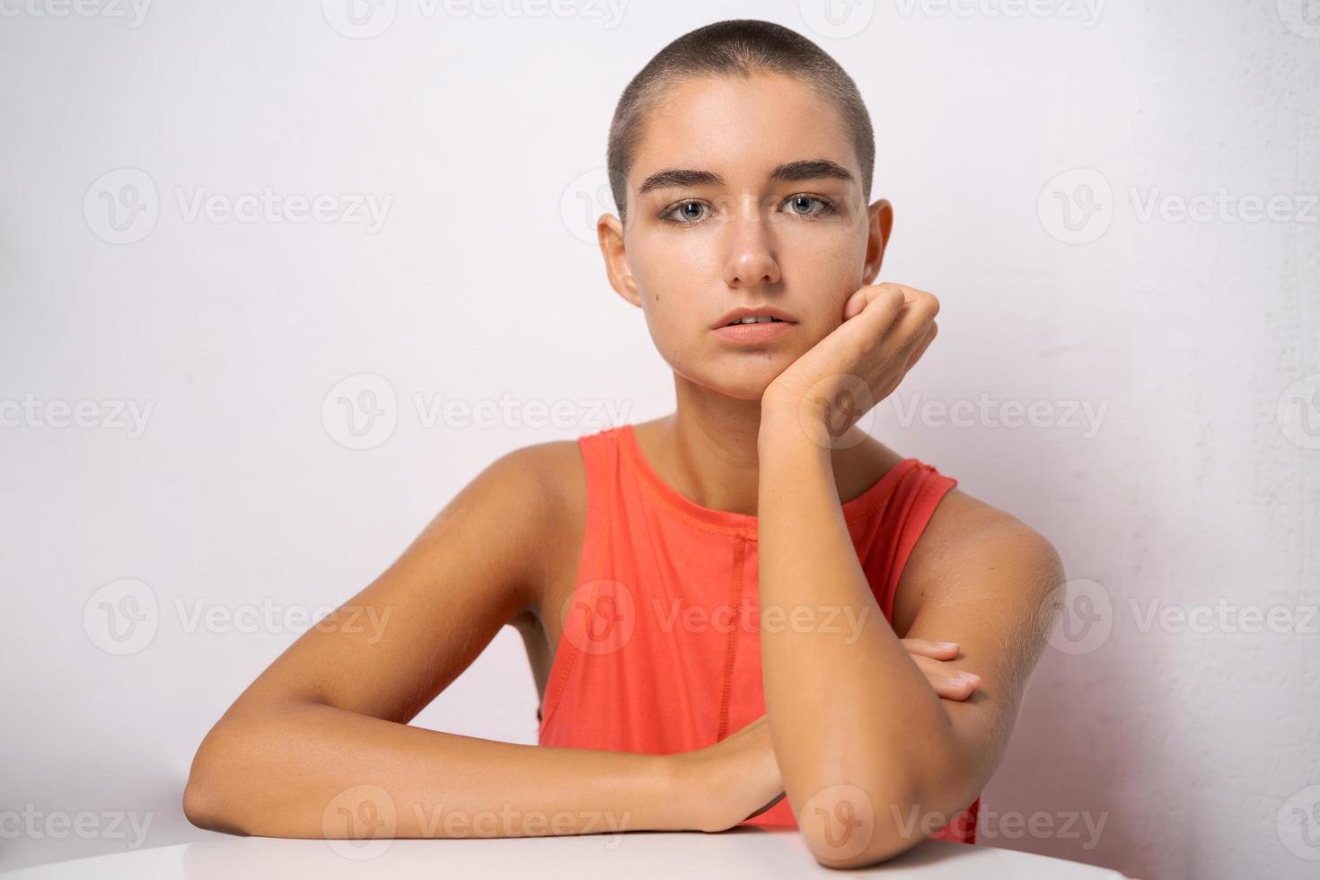 Kaukasisches Mädchen mit kurzen Haaren, fast kahl, hält ihre Hände hinter dem Kopf foto