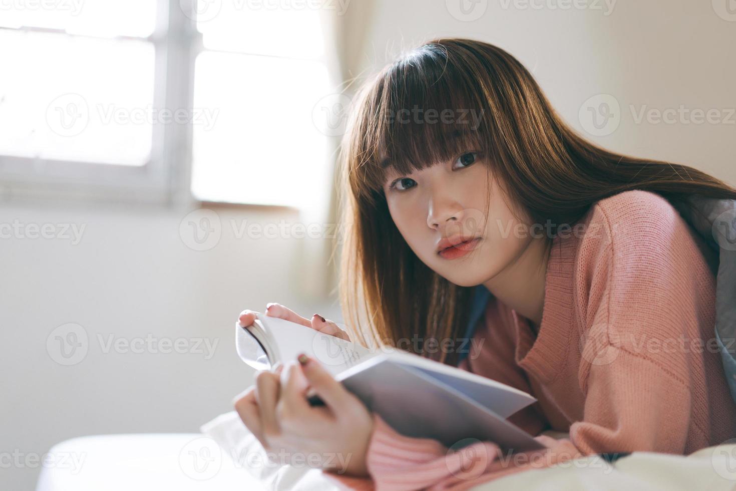Porträt junge asiatische nette Frau jugendlich College-Student, der am Morgen ein Buch im Schlafzimmer liest. foto