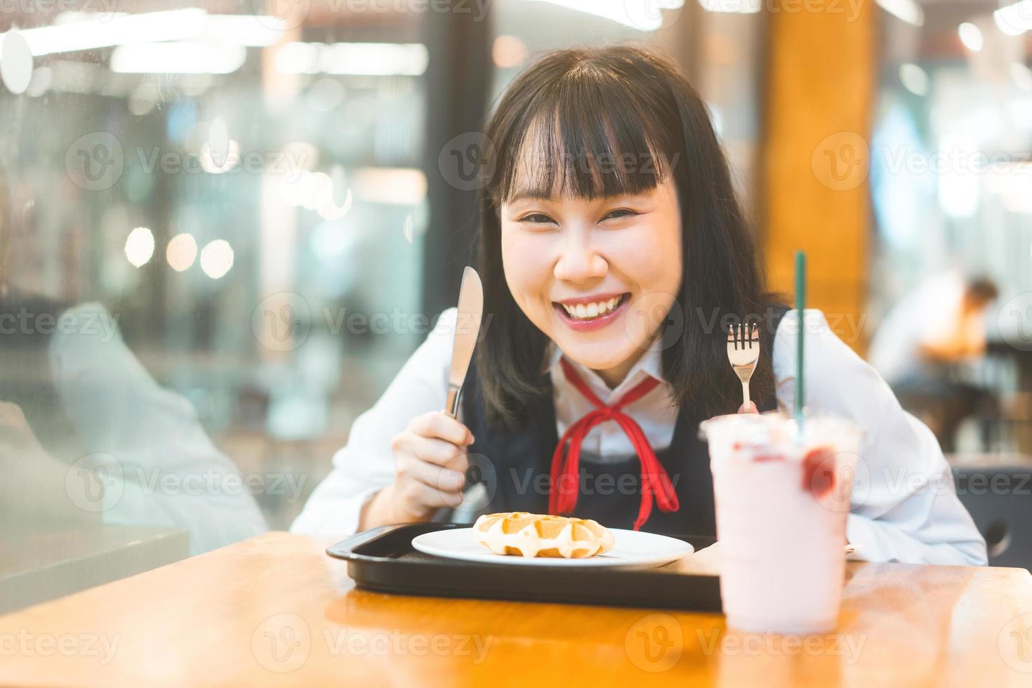 glückliche junge asiatin in japanischer uniform studentin im café mit waffel foto