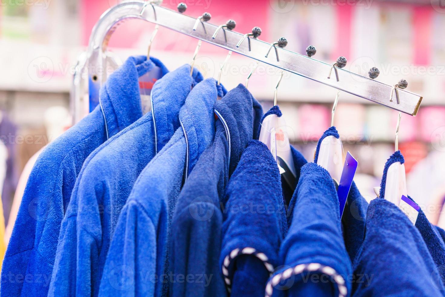 Blaue Frottee-Bademäntel hängen an Kleiderbügeln in einem Geschäft, Nahaufnahme selektiver Fokus. foto