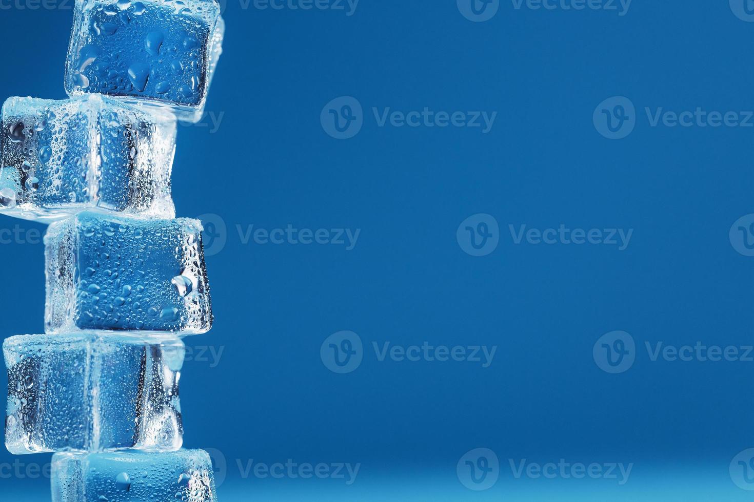 Eiswürfel mit Wassertropfen ragen in einer Reihe auf blauem Grund auf. foto