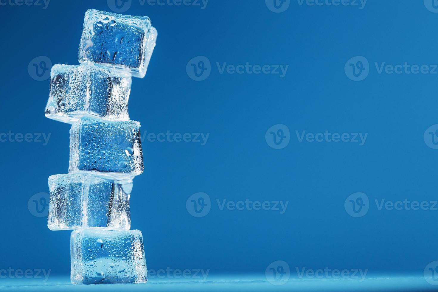 Eiswürfel mit Wassertropfen ragen in einer Reihe auf blauem Grund auf. foto