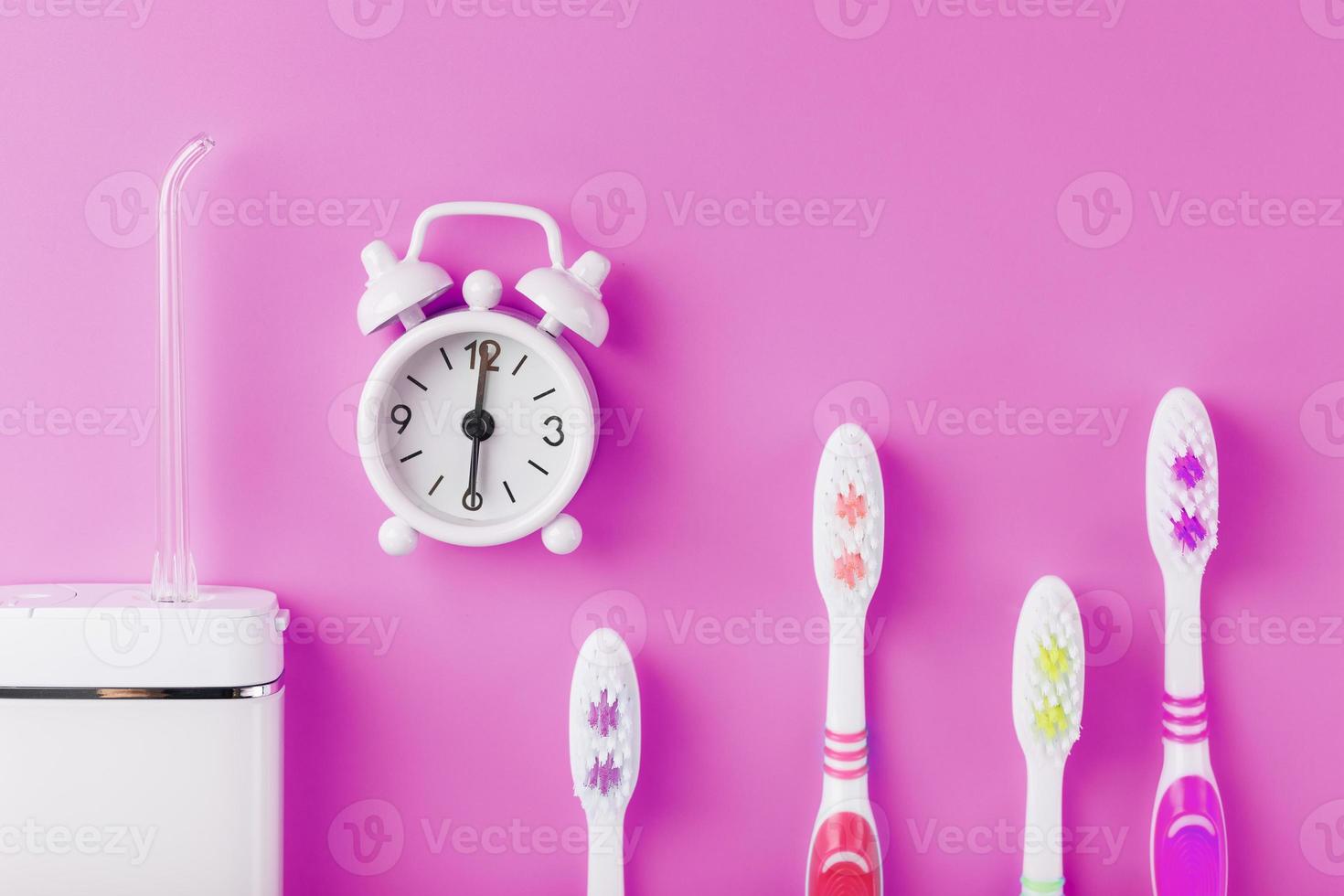 Ein Irrigator zum Zähneputzen auf rosafarbenem Hintergrund mit Uhr und Zahnbürsten. foto