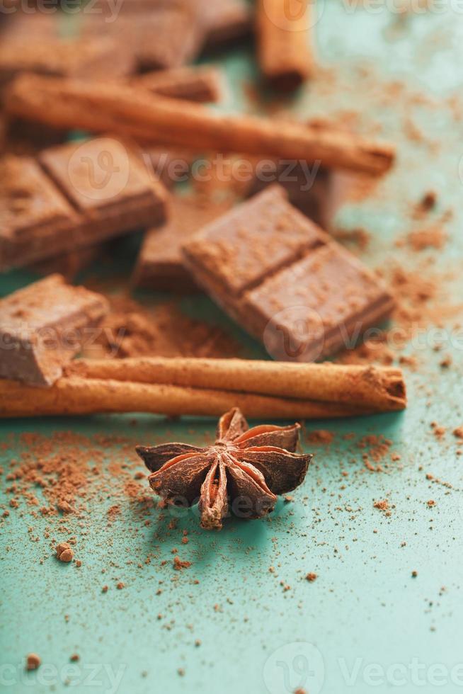 Schokolade in Scheiben gebrochen mit Kakaopulver und Gewürzen auf grünem Hintergrund foto