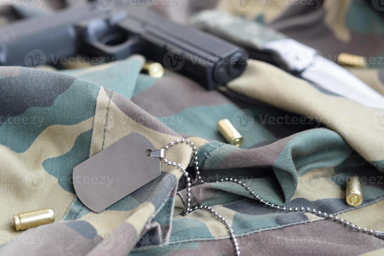 Army Dog Tag Token mit 9-mm-Kugeln und Pistole liegen auf gefaltetem, tarngrünem Stoff foto