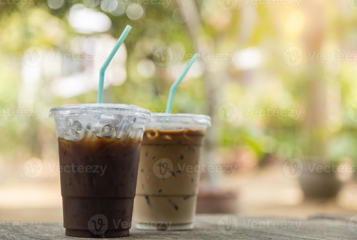 Nahaufnahme von Plastikbechern mit Eiskaffee Americano und Eiskaffee Latte auf Holztisch im Garten zum Mitnehmen foto