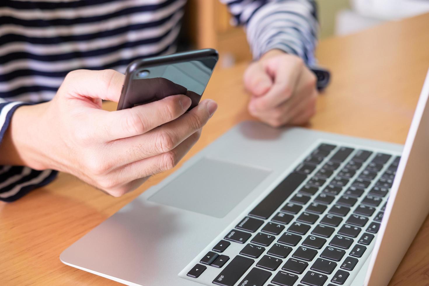 männer hand mit handy vor seinem computer laptop auf holztisch zu hause. Hochgeschwindigkeits-Internettechnologie ermöglicht es Menschen, auf Unterhaltung und Online-Inhalte zuzugreifen oder mit Sicherheit zu arbeiten. foto