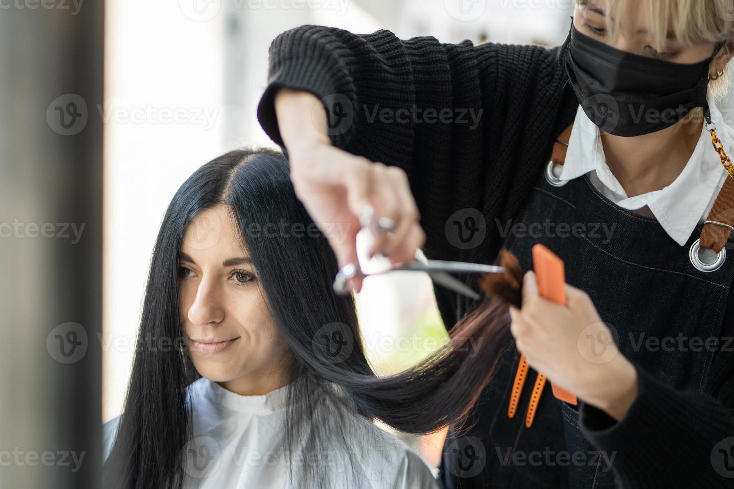 kaukasische frauen mit stilvollem haar, während sie haare schneiden und eine chirurgische gesichtsmaske tragen, während sie haare für den kunden stylen. Berufliche Tätigkeit, Schönheits- und Modeservice neue Normalität foto