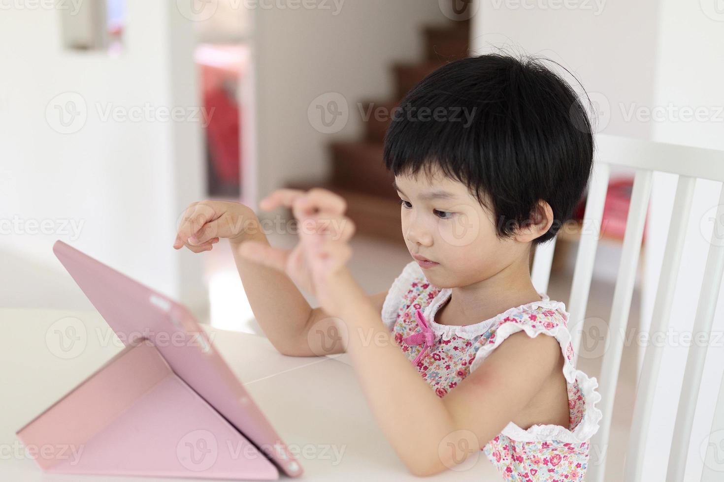 kleines asiatisches mädchen, das zu hause digitales tablet spielt foto