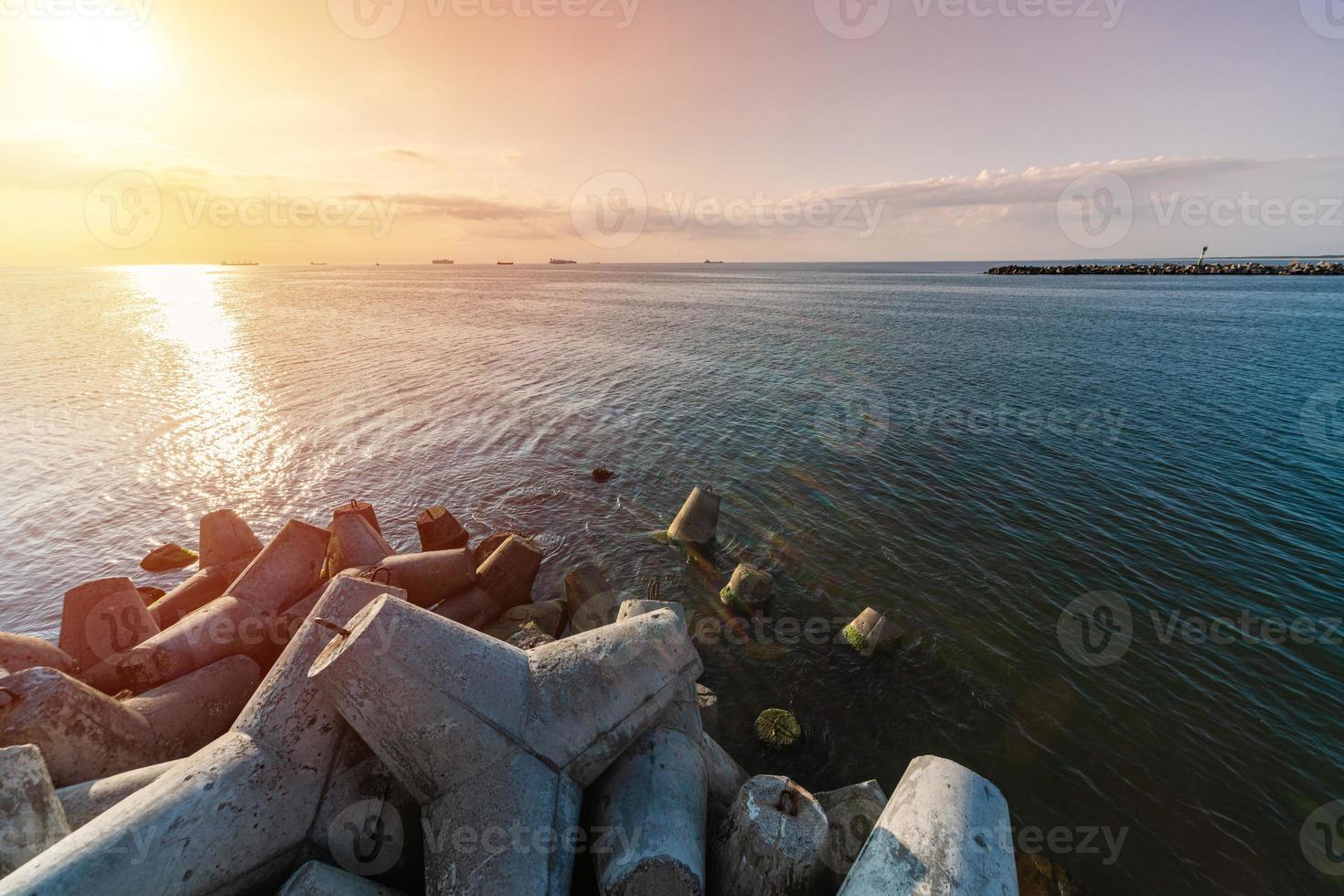 schöne sonnenuntergang seelandschaft. Reiseträume und Motivation. Wellenbrecher Tetrapoden am Ufer des Piers. Frachtschiffe am Horizont. foto