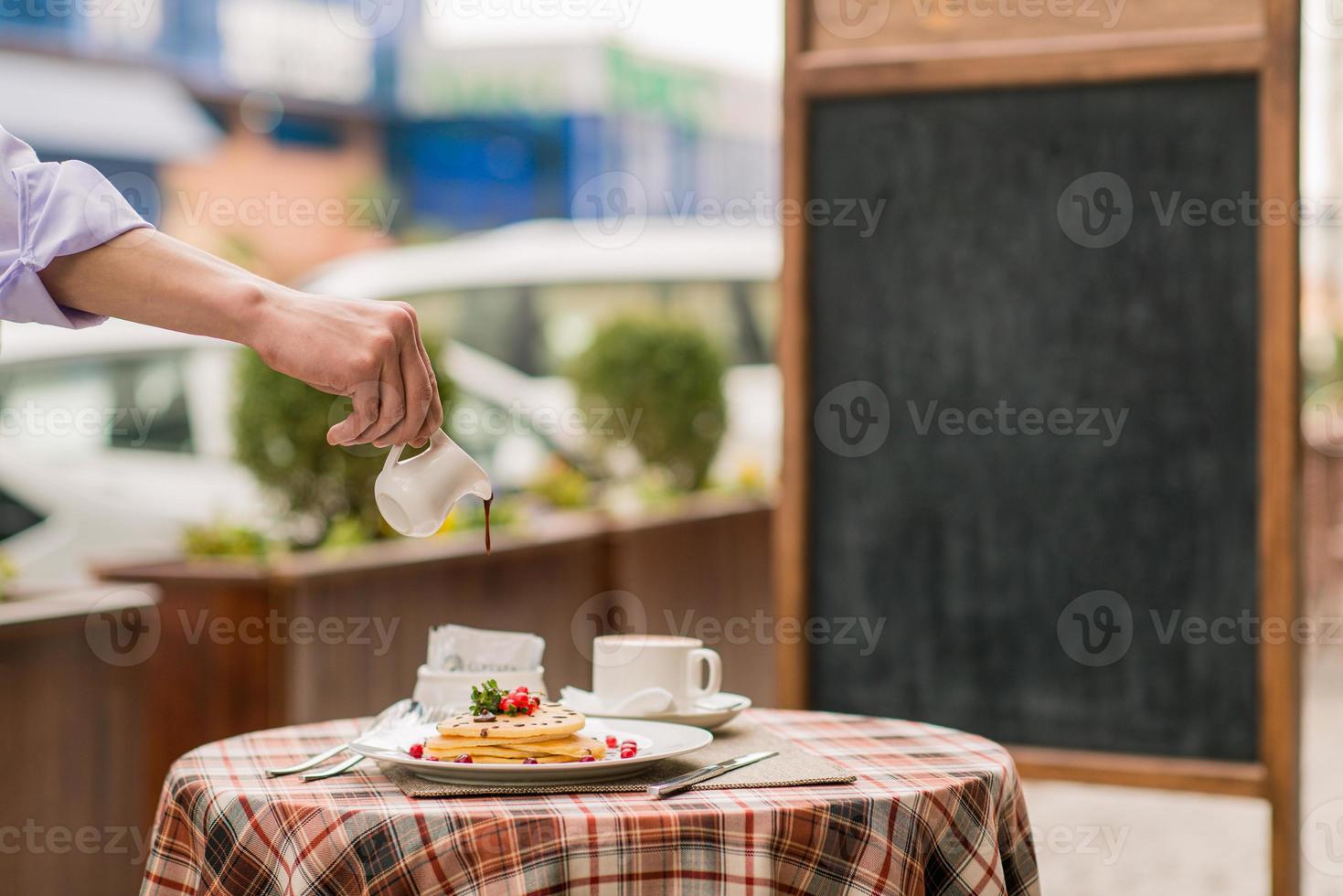 Der Koch gießt Sirup auf Pfannkuchen mit Beeren auf dem Serviertisch zum Frühstück foto