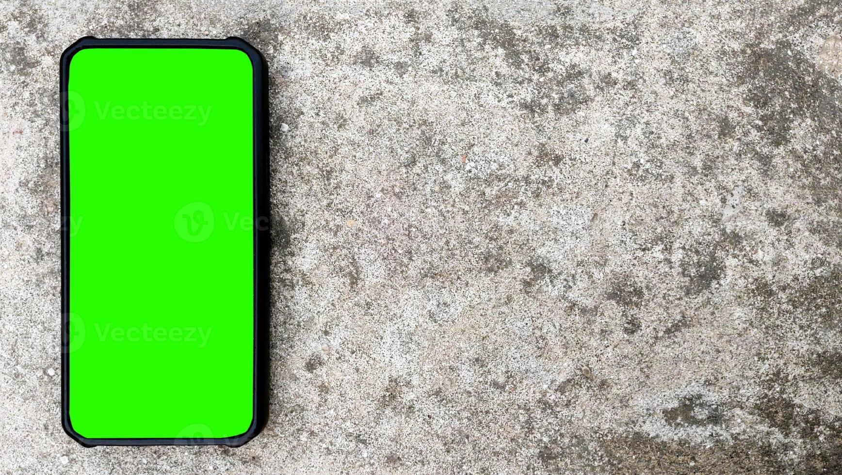 Draufsicht eines schwarzen Smartphones mit grünem Bildschirm auf konkretem Hintergrund. Platz für Text kopieren foto