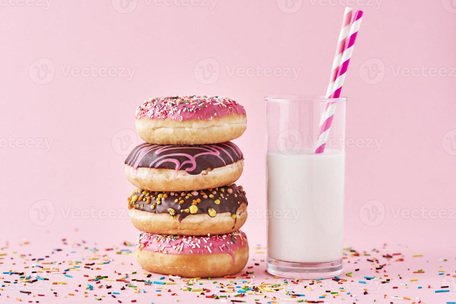 Stapel bunter Donuts dekoriert und Glas Milch auf rosa Hintergrund foto