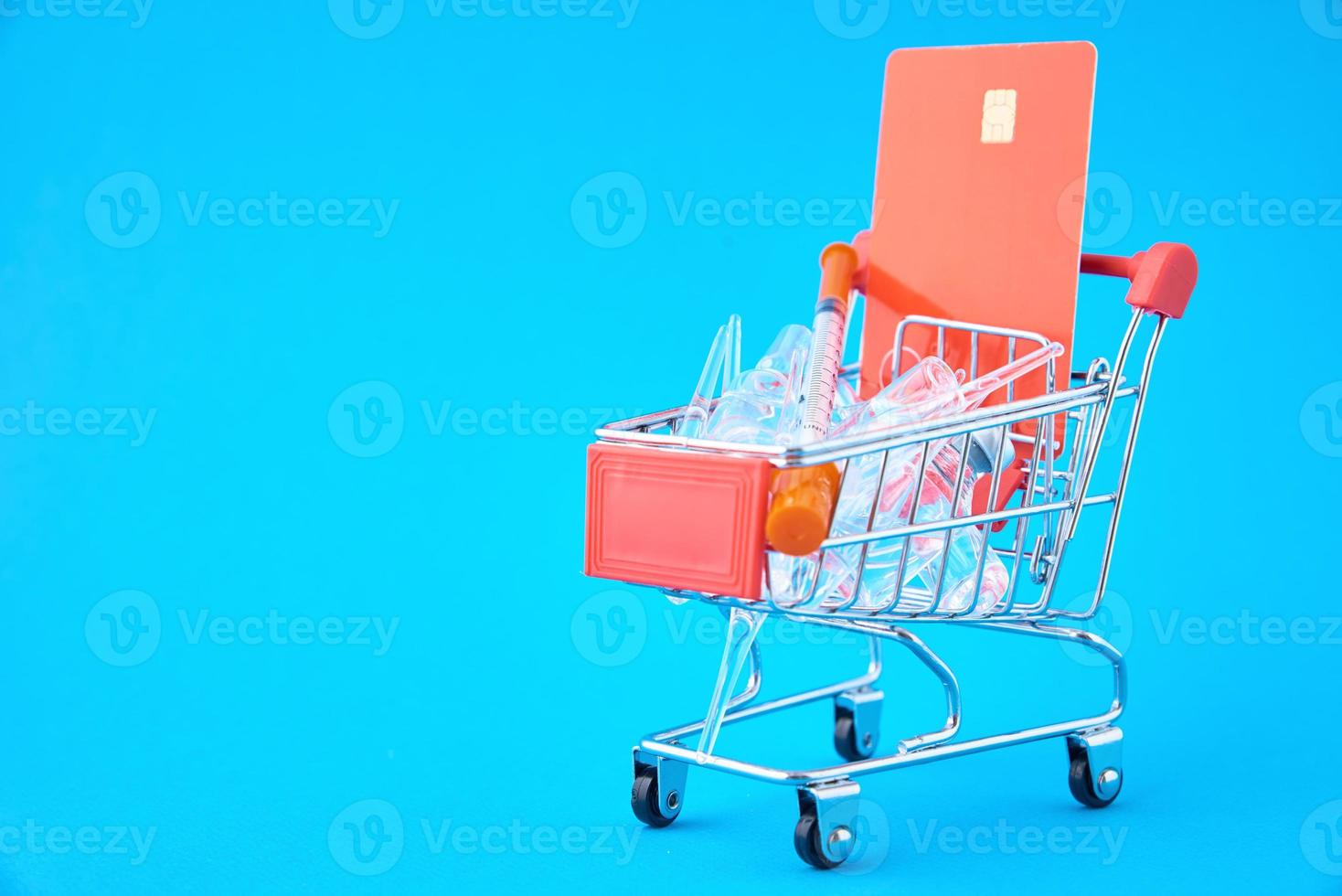 Spritzen und Ampullen mit Medikamenten im Einkaufswagen auf blauem Hintergrund foto
