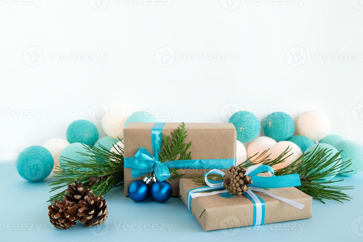 zwei weihnachtsgeschenkboxen aus bastelpapier, blaue und weiße bänder, verziert mit tannenzweigen, tannenzapfen und weihnachtskugeln auf dem blau-weißen hintergrund mit weihnachtslichtern. foto