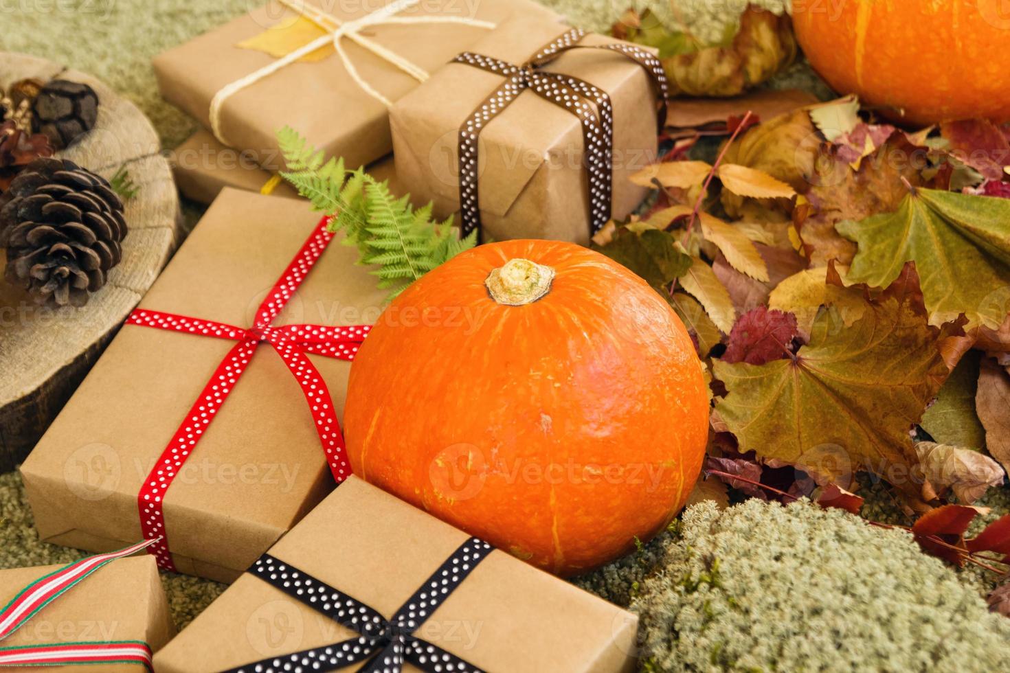 Herbststillleben mit Kürbissen, Geschenkboxen aus Bastelpapier und bunten Bändern, trockenen Blättern, trockenem Moos, Farnblättern und Tannenzapfen auf grünem Hintergrund. foto