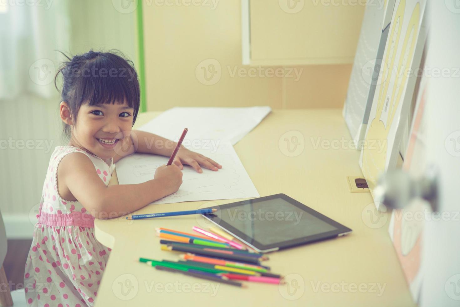kleines asiatisches kind, das mit einem bleistift auf notizbuch am schreibtisch schreibt foto