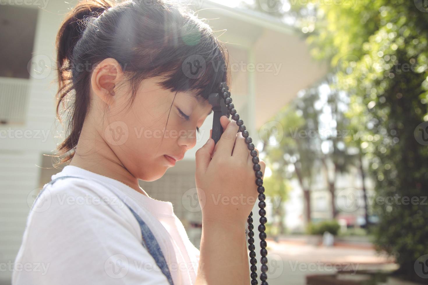 Kleines asiatisches Mädchen, das mit dem Halten des Kreuzes betet, christliches Konzept. foto