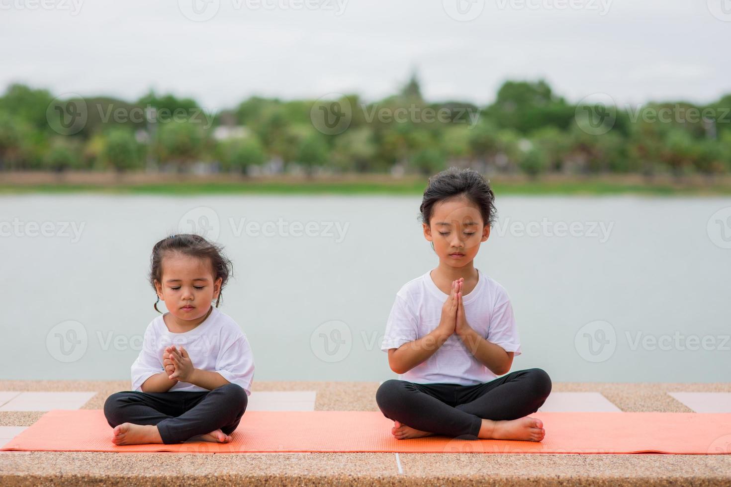 kleines süßes asiatisches mädchen, das yoga-pose auf einer matte im park praktiziert, gesundes und übungskonzept foto