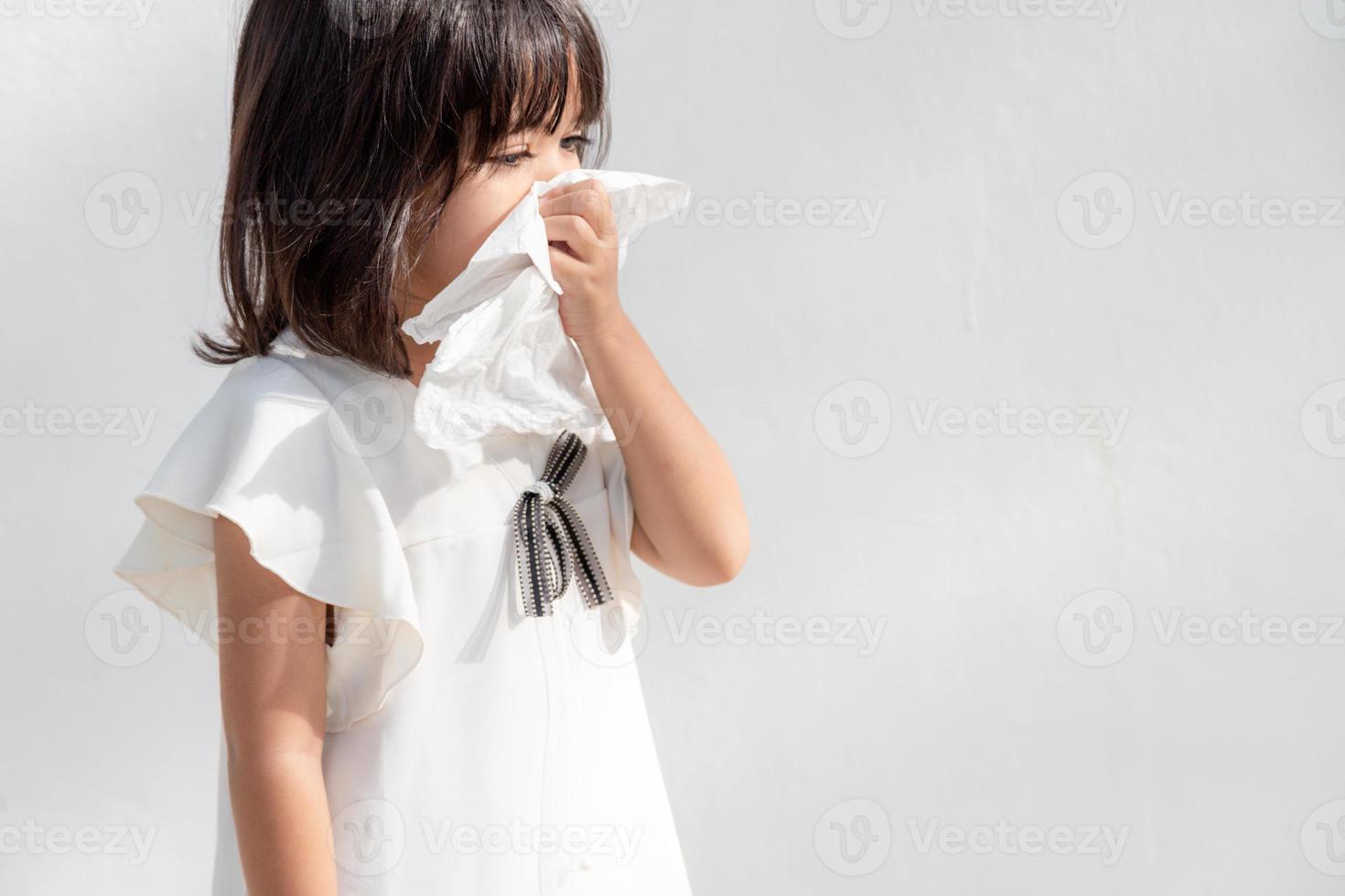 asiatisches kind mädchen krank mit niesen auf der nase und kaltem husten auf seidenpapier, weil schwach oder virus und bakterien durch staubwetter und kindergarten und vorschule foto