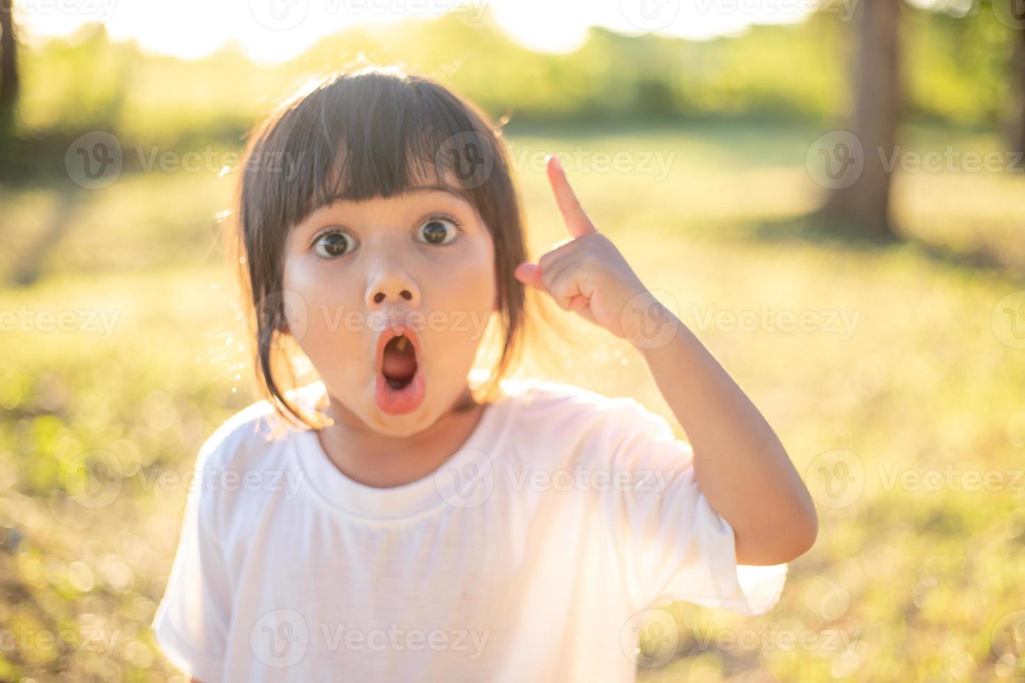 Asiatisches kleines Mädchen, das mit dem Finger lächelt und nach oben zeigt foto