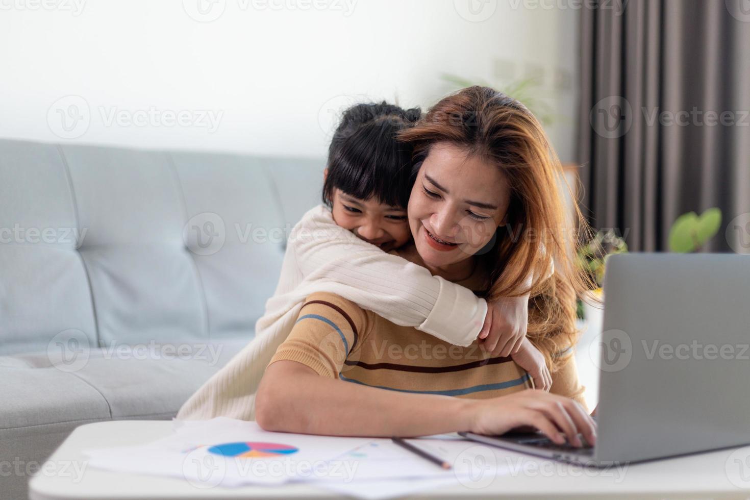 kleines Mädchen, das ihrer Mutter einen Kuss gibt, während sie von zu Hause aus arbeitet foto