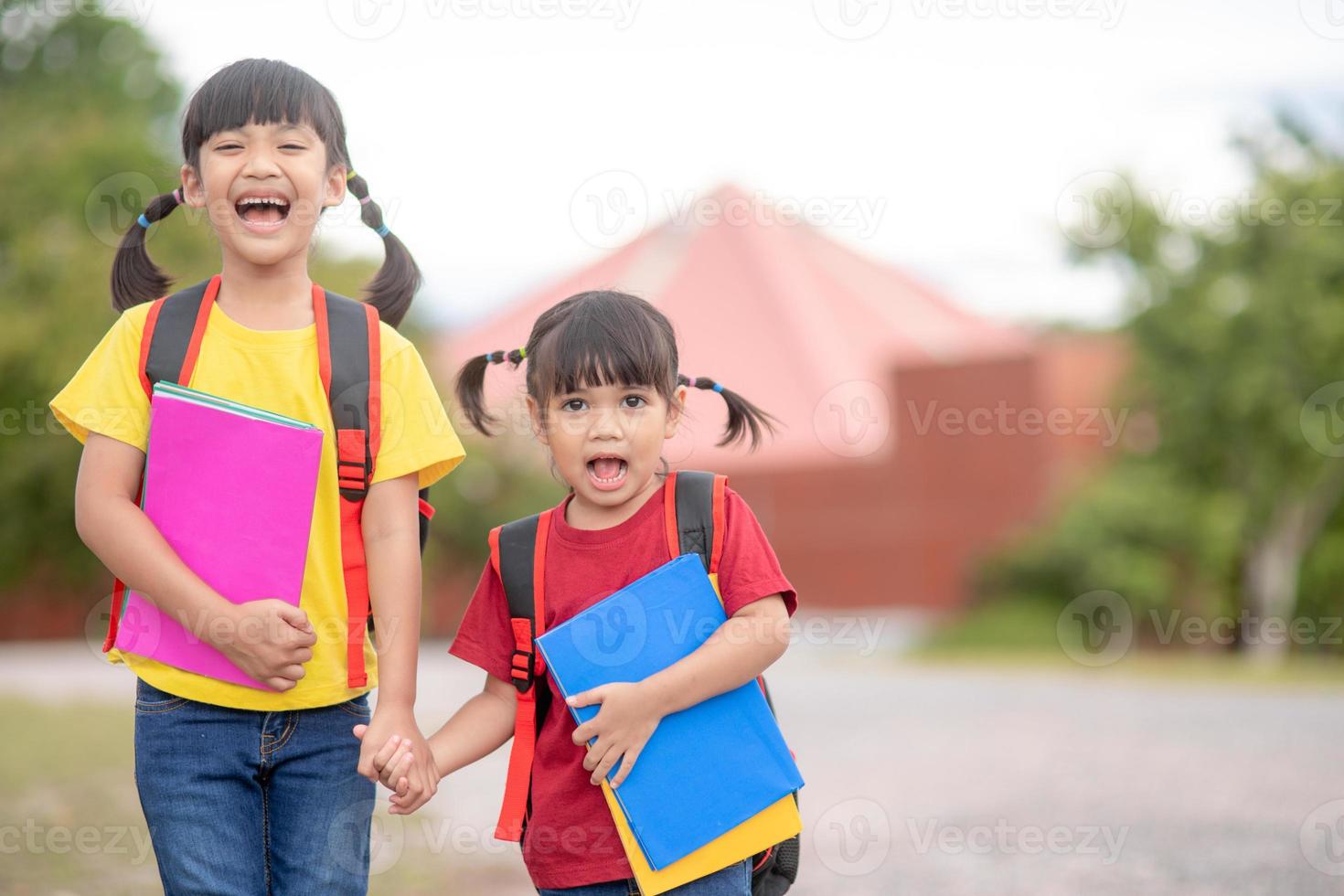 zurück zur Schule. Zwei süße asiatische Mädchen mit Schultasche, die ein Buch in der Schule zusammenhalten foto