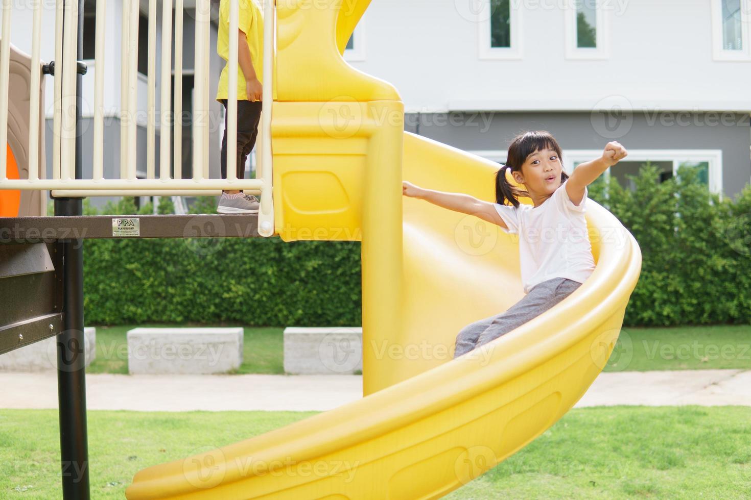 Kind spielt auf Spielplatz im Freien. kinder spielen auf dem hof der schule oder des kindergartens. aktives kind auf bunter rutsche und schaukel. gesunde sommeraktivität für kinder. foto