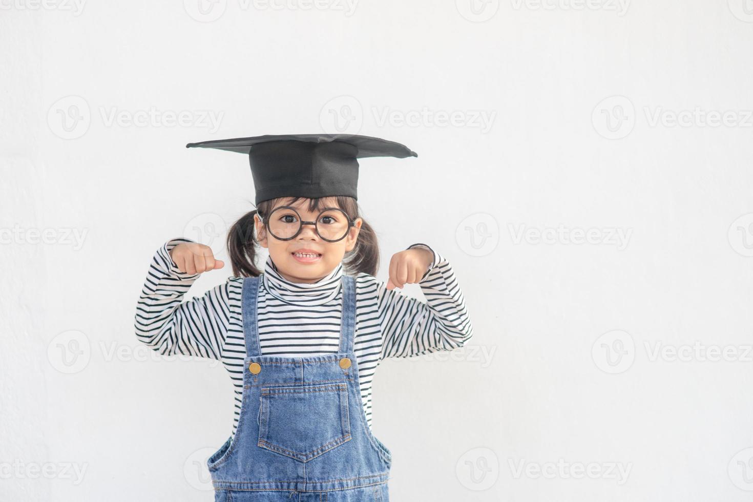 Kinder Mädchen, das eine graduierte Kappe über weißem Hintergrund trägt, sind sehr glücklich und aufgeregt und machen Gewinnergesten mit erhobenen Armen, lächeln und schreien nach Erfolg. feierkonzept. foto