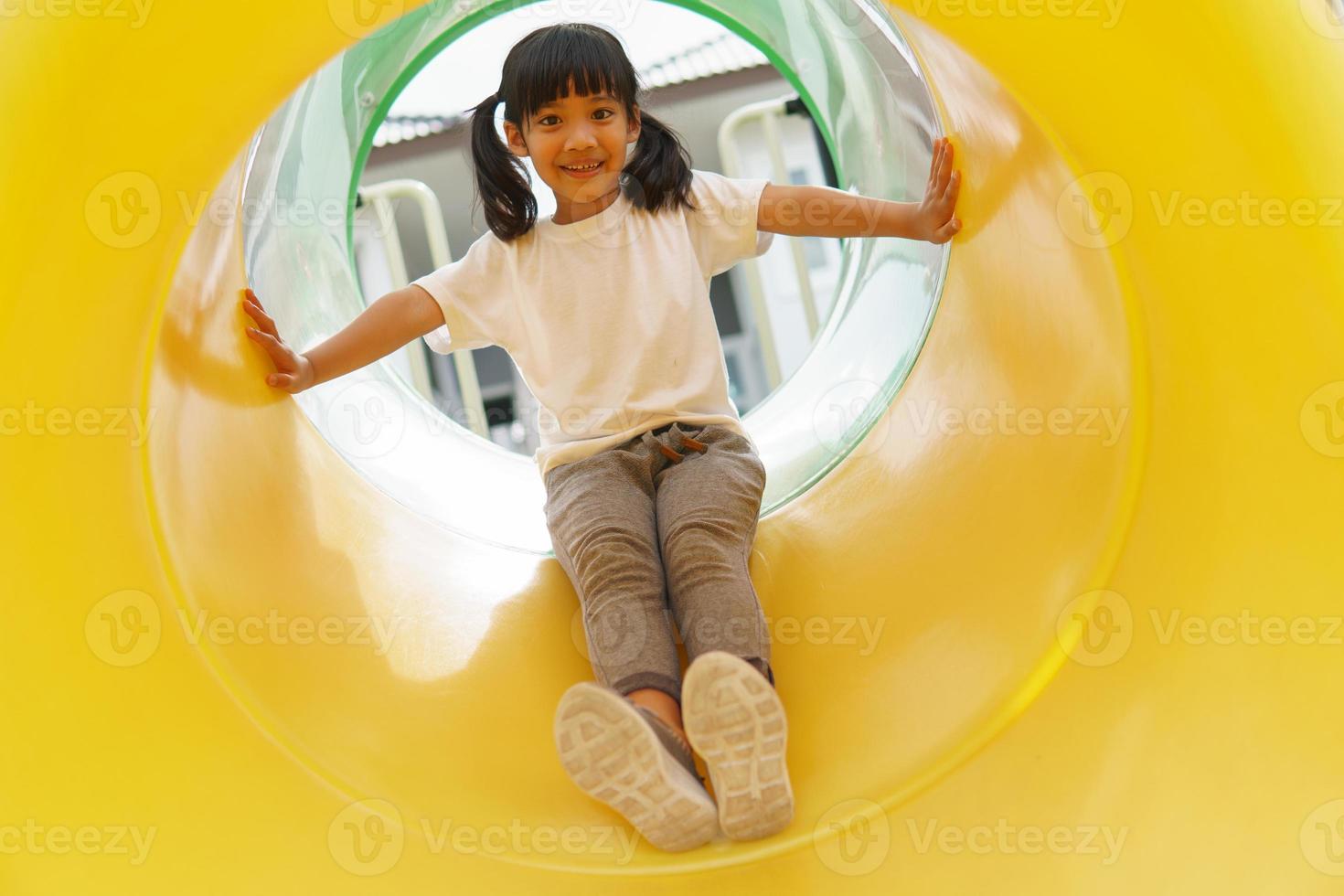 Kind spielt auf Spielplatz im Freien. kinder spielen auf dem hof der schule oder des kindergartens. aktives kind auf bunter rutsche und schaukel. gesunde sommeraktivität für kinder. foto