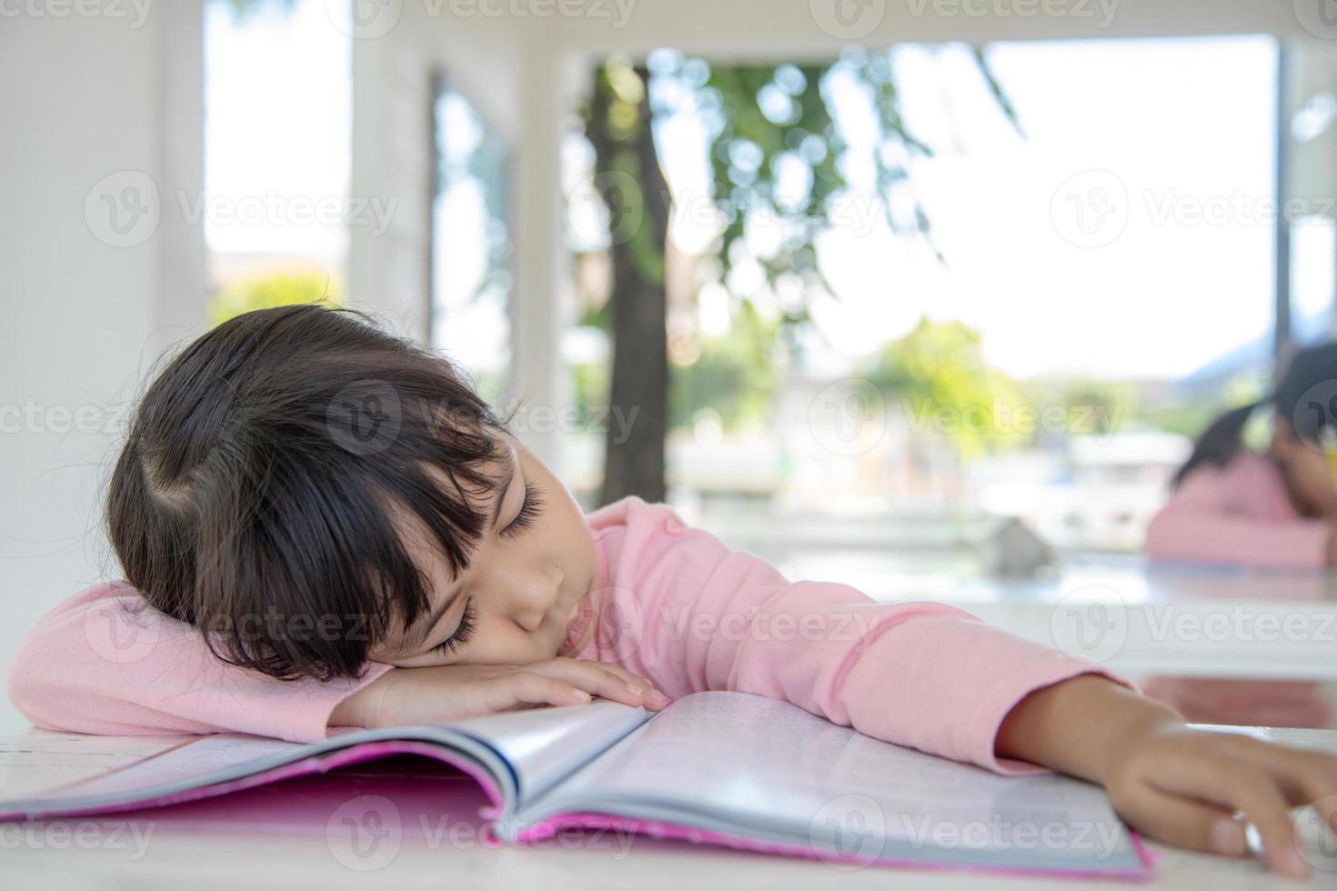 Kleines asiatisches Mädchen, das auf dem Schreibtisch im Klassenzimmer schläft foto