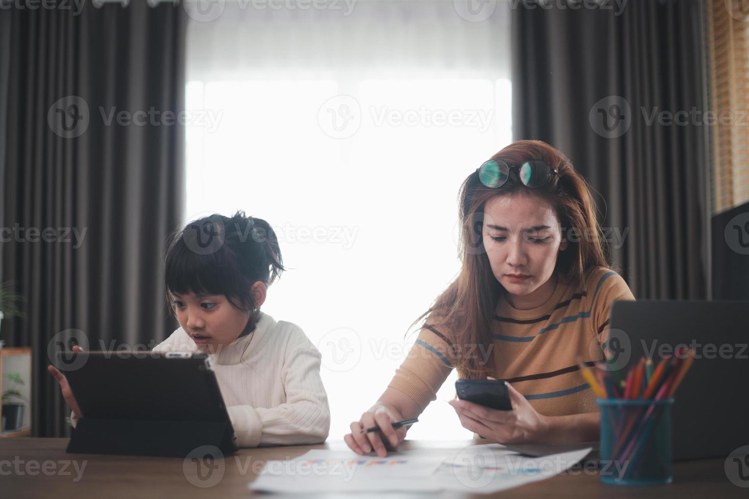 Mutter arbeitet und ihre Tochter. während ihre Tochter Tablet spielt. arbeitsreicher Tag der Mutter. das tägliche lebenskonzept der mutter foto