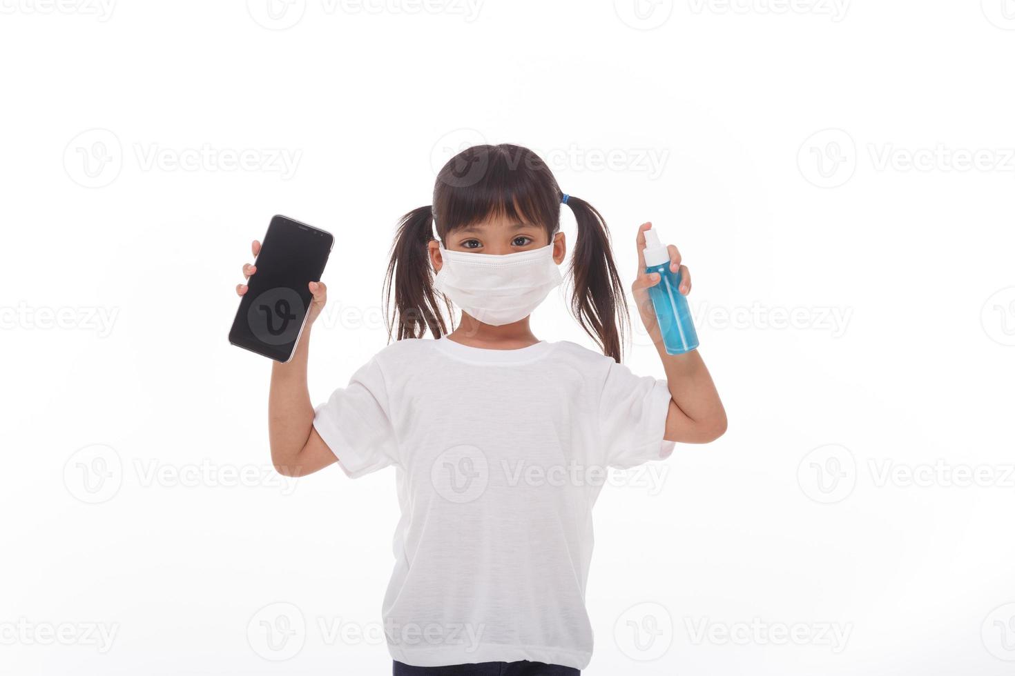 asiatische mädchen tragen eine maske, die den smartphone-bildschirm mit alkohol reinigt. auf weißem hintergrund. konzept der reinigung von schmutzigen bildschirmtelefonen zur krankheitsprävention durch bakterien. foto