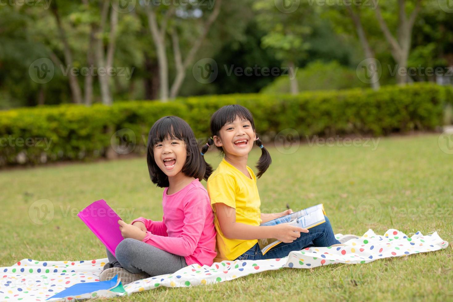 Zwei schöne kleine Mädchen, die Bücher im Garten lesen, sitzen auf Gras. das konzept von bildung und freundschaft. foto