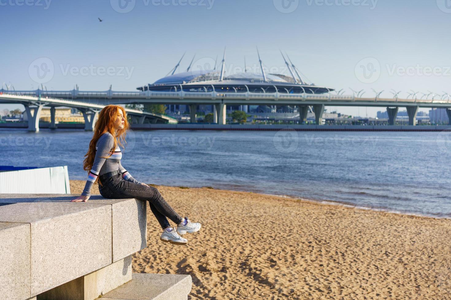 Schöne rothaarige junge Frau sitzt an einem Frühlingstag auf dem Damm foto