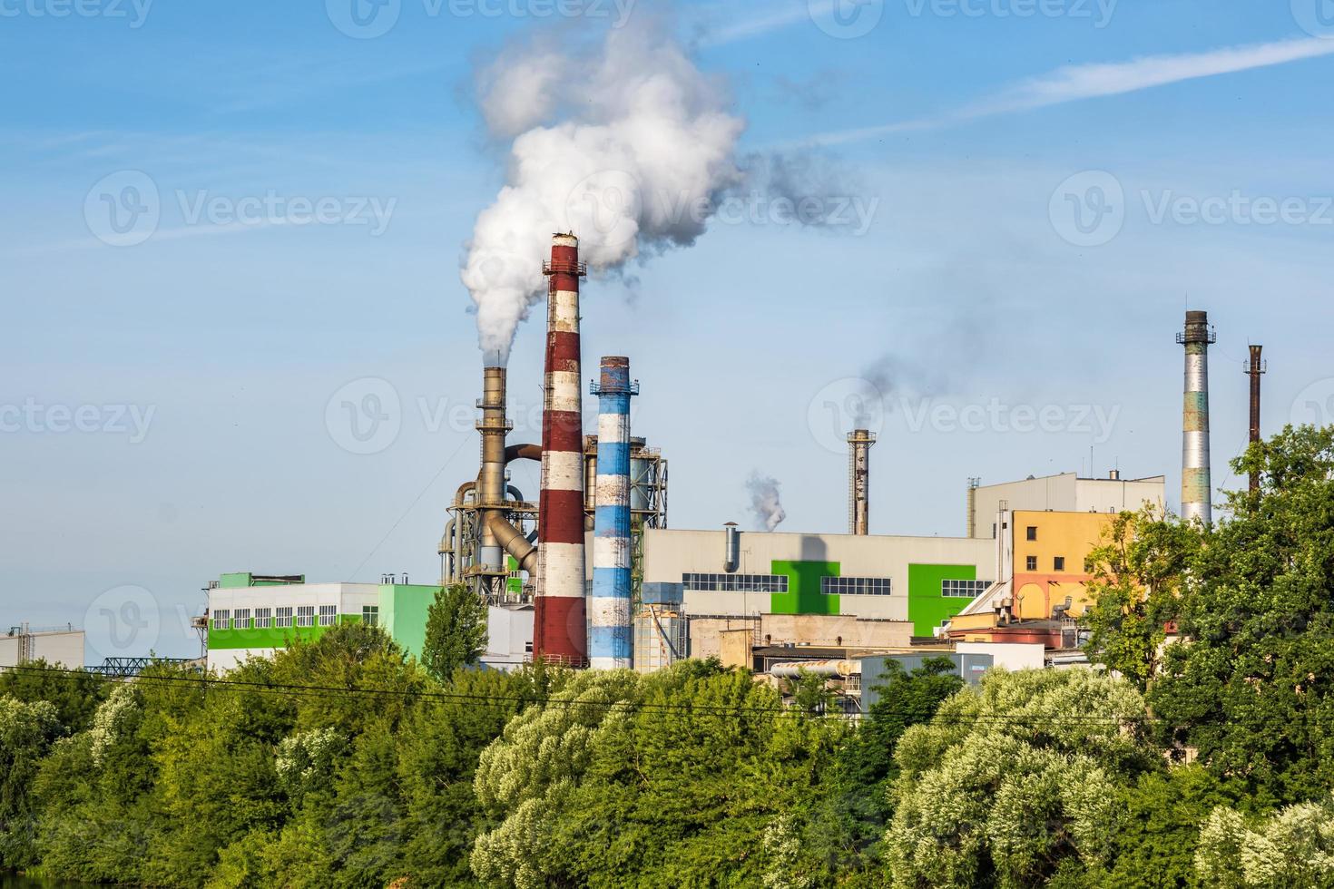 Rohre des Sägewerks des Holzbearbeitungsunternehmens mit schöner Spiegelung im blauen Wasser des Flusses. Luftverschmutzungskonzept. Industrielandschaft Umweltverschmutzung Abfall von Wärmekraftwerken foto