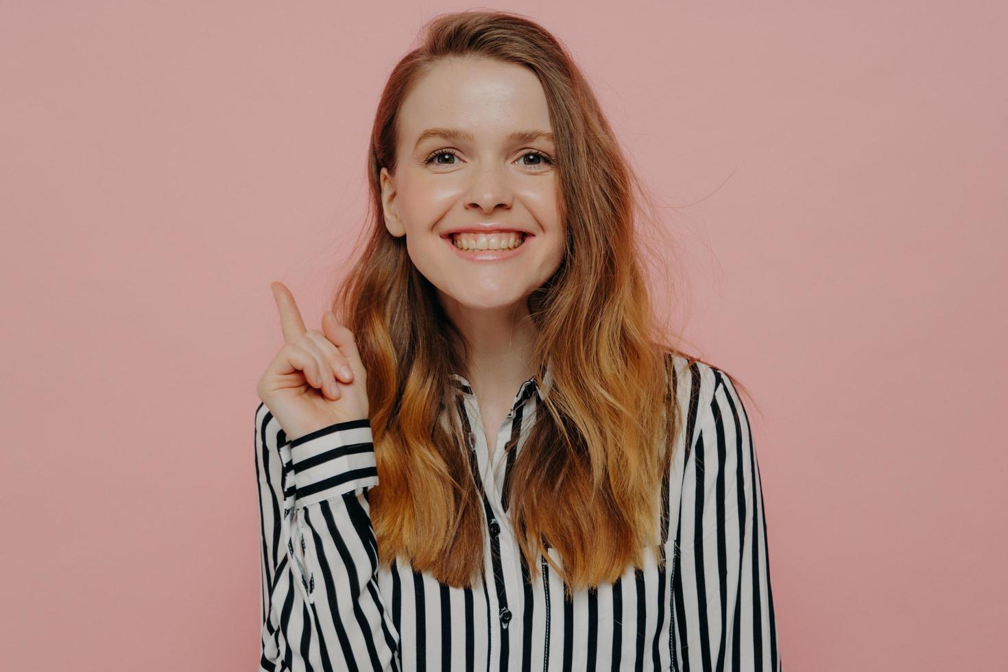 glückliches Teenager-Mädchen, das mit dem Zeigefinger auf den Kopierbereich zeigt und lächelt foto