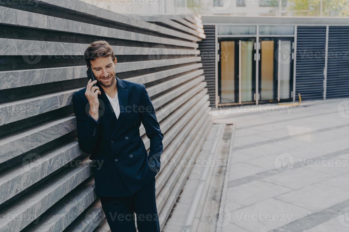 CEO-Mann, der ein angenehmes Telefongespräch auf dem Handy führt, während er außerhalb des Eingangs des Bürozentrums steht foto