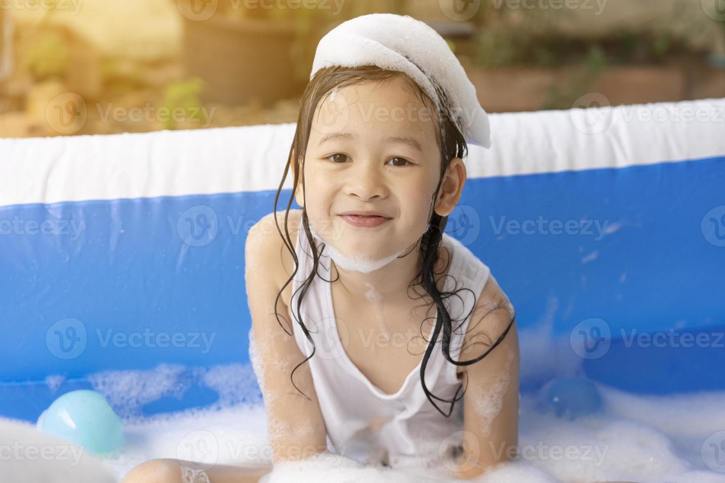 Schönes asiatisches Mädchen, das in einem aufblasbaren Pool spielt. im Sommer zu Hause im Wasser spielen. Seifenblasenspiel, Familienglück, im Wasser spielende Kinder foto